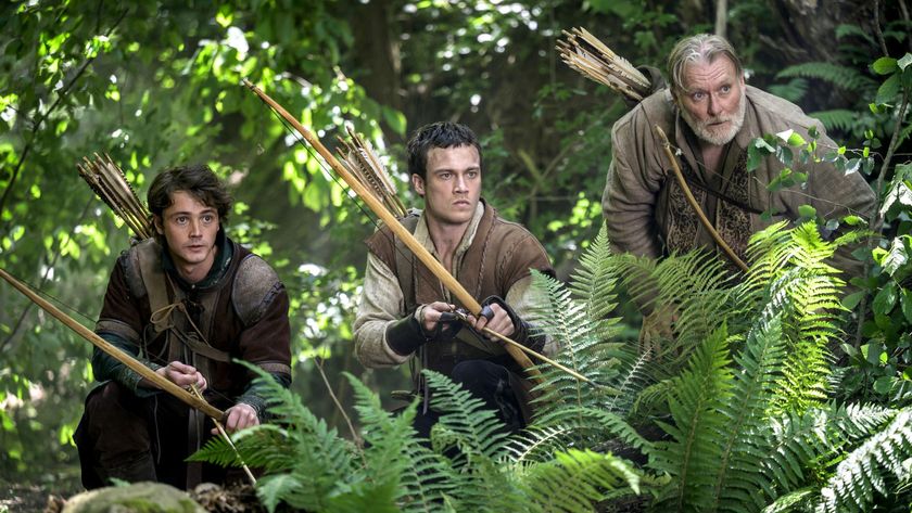 Robin Hood and two Merry Men draw their bows while hiding in the woods