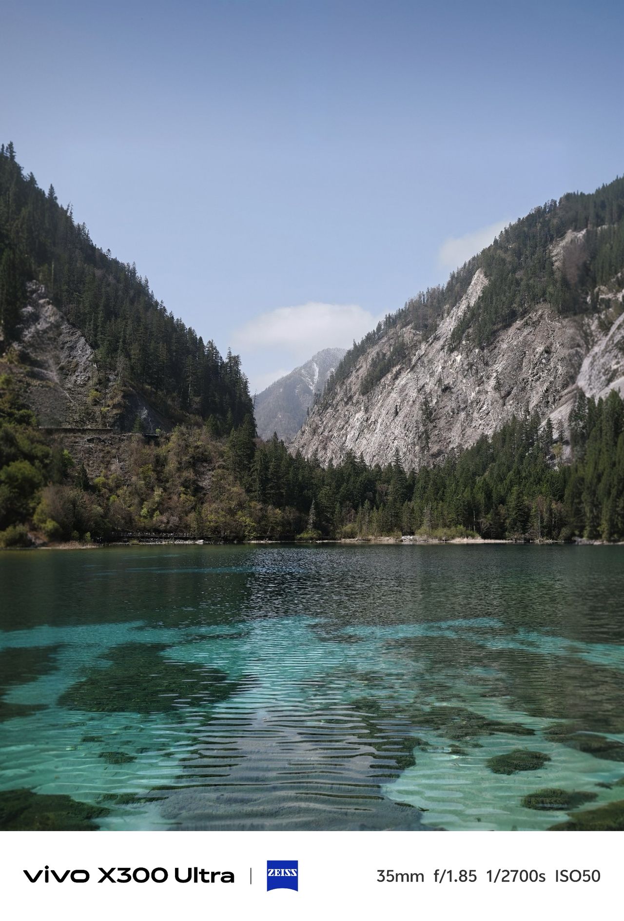 Clear turquoise lake surrounded by forested mountains and rocky cliffs, photographed on the Vivo X300 Ultra.