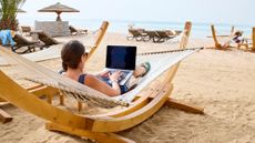 A woman typing on her laptop while in a hammock on beach