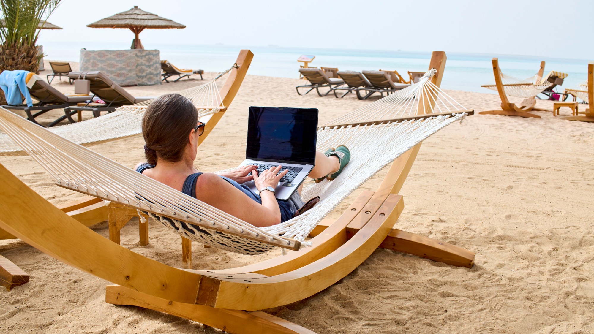 A woman typing on her laptop while in a hammock on beach