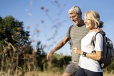 Smiling mature couple with backpacks hiking in forest on sunny day