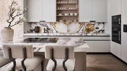 kitchen with marble worktops, streamlined taupe handless cabinets and drawers and island with cream barstools