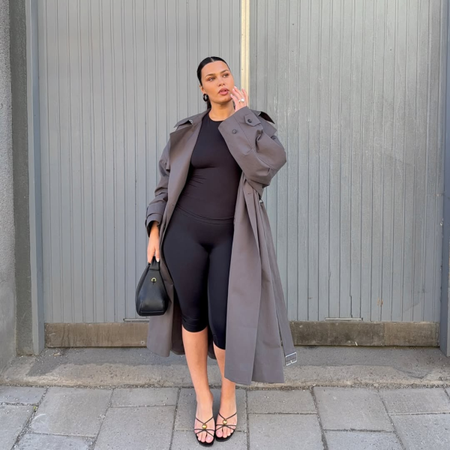 Isabelle in a grey trench coat, black capris and black strappy heeled sandals