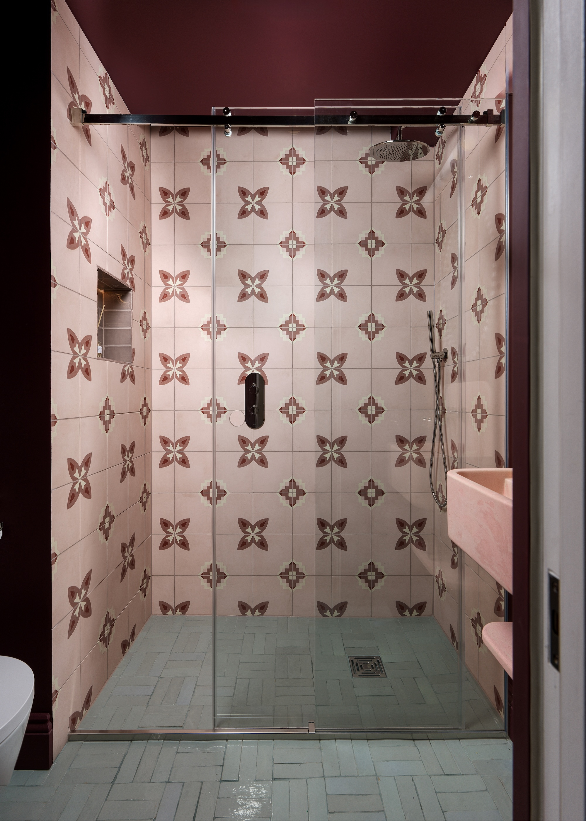 A walk-in shower with a glass front, pale pink patterned tiles on the walls, and a burgundy painted ceiling