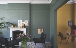 A living room with dark green walls, and an adjoining room with yellow walls