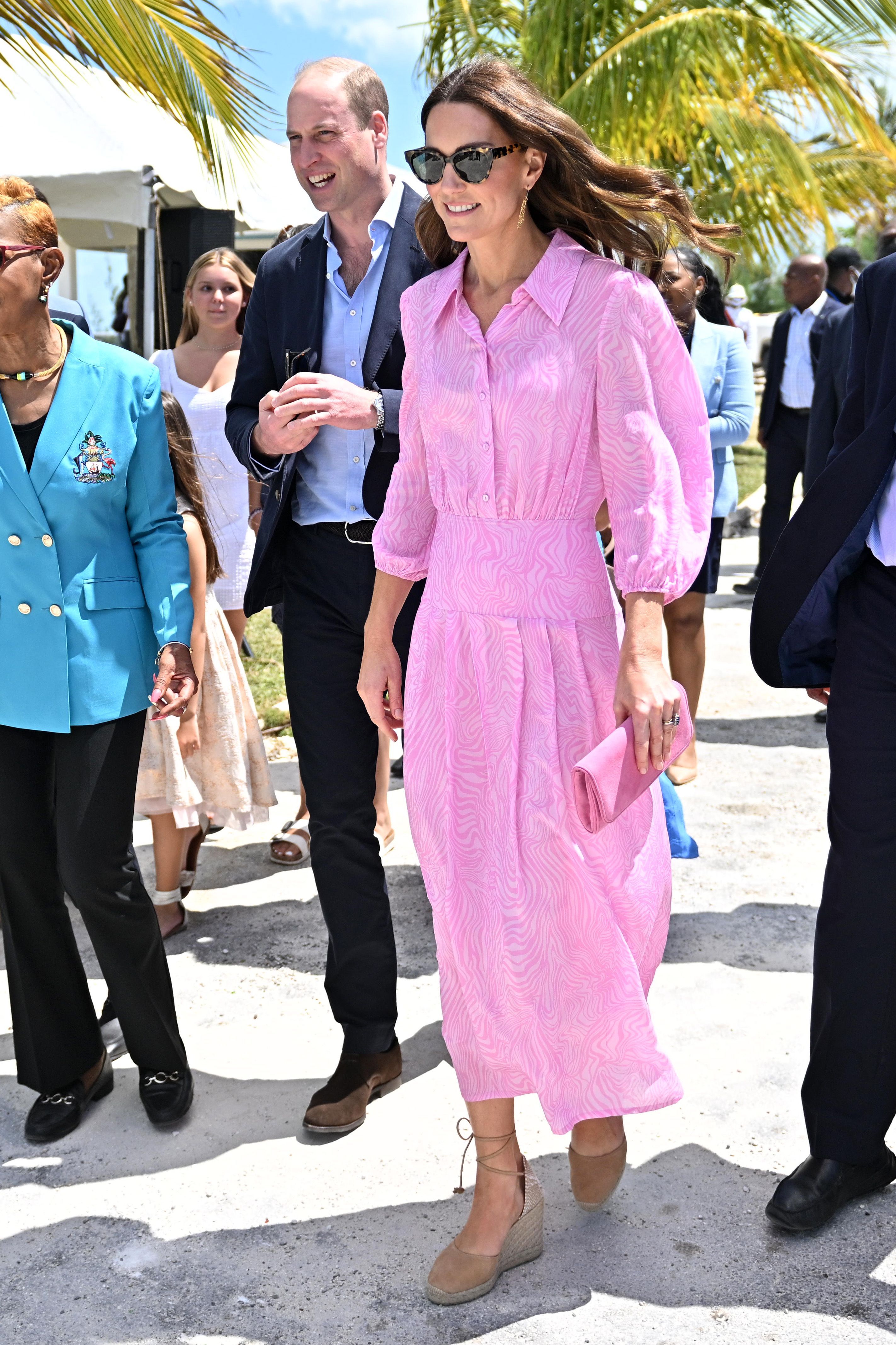 Princess Kate wearing a pink dress walking in front of a palm tree