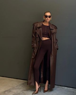 Model Elsa Hosk wears brown stirrup leggings with matching brown trench coat, cardigan, heels and sunglasses.