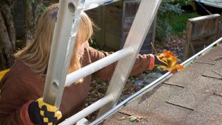woman using ladder to clean gutters