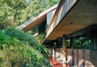 Exterior of concrete house with lush greenery, concrete pillars, red floors and exposed plumbing