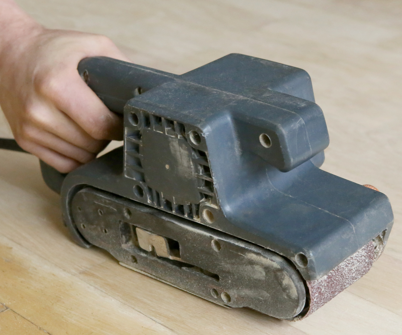 A belt sander being used to sand a wood floor.