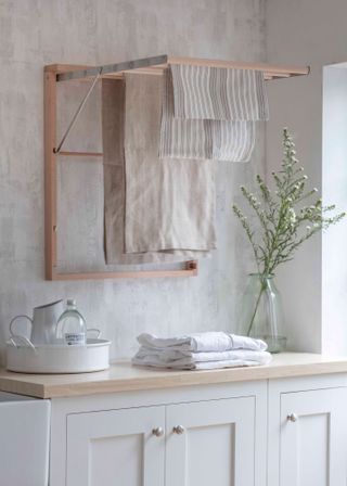 Small laundry room ideas featuring a fold-out wooden drying rack in a white and neutral scheme with a large vase of flowers.