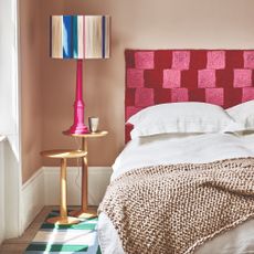 A beige-painted bedroom with a crochet cequered headboard and a colourful table lamp on the bedside table