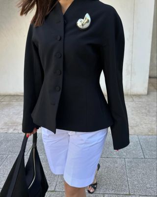 Debora Rosa mengenakan blazer hitam, celana pendek putih, dan bros Zara berwarna perak.