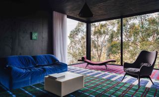 Seating area featuring a blue velour sofa, coffee table and chair with a vibrant geometric rug