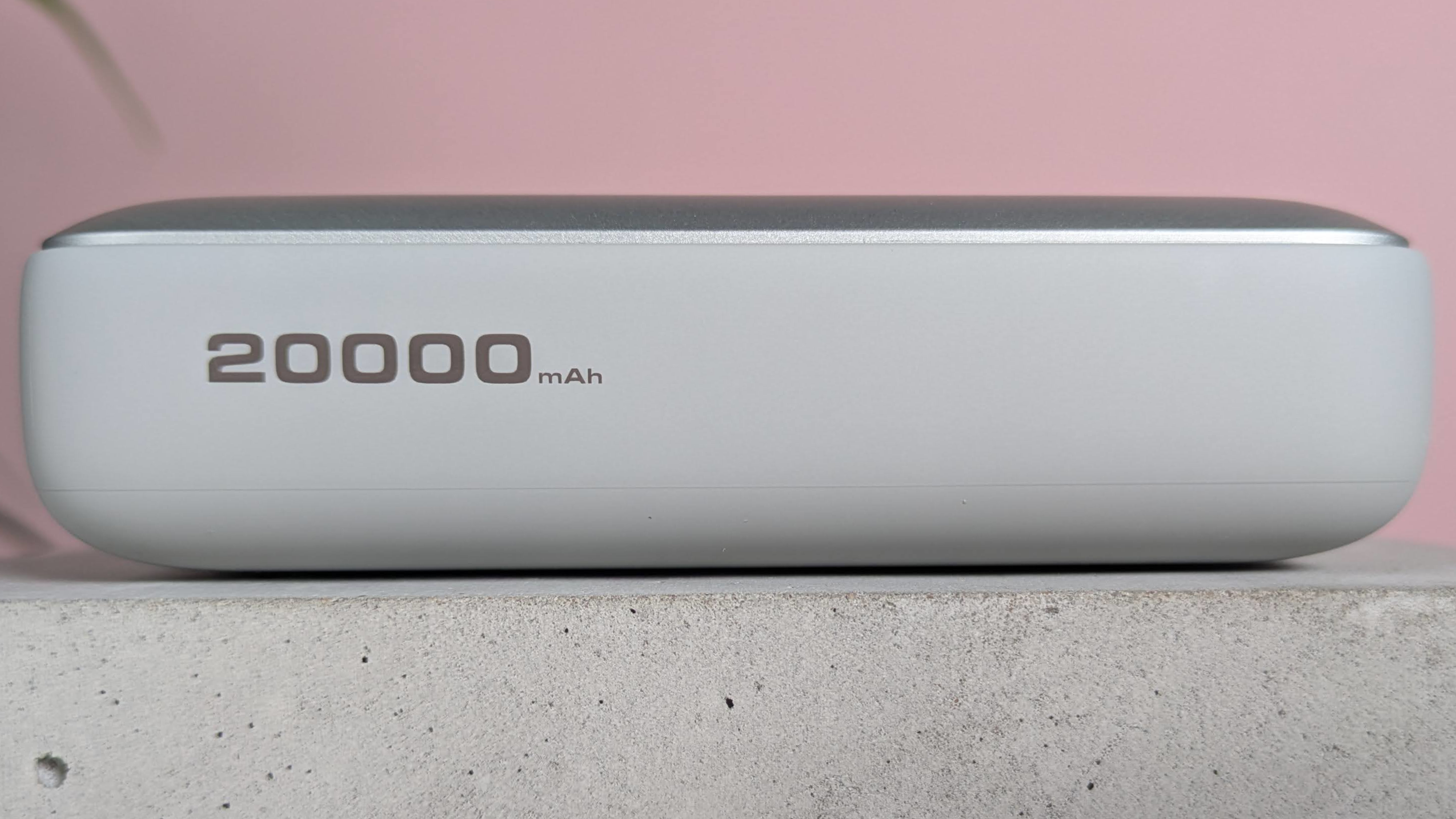 Side view of Aukey Spark Mini 20000 on plinth with pink wall and plant in background