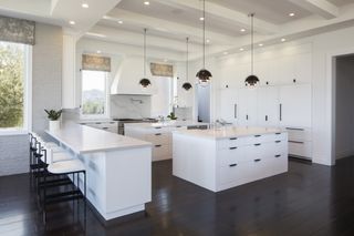 A white kitchen with dark floors and black pendant lights
