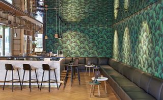 Large bar area with leather seating along the entirety of one wall, mirrored ceiling and botanical-style wallpaper