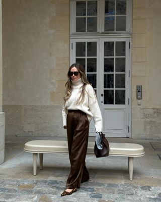 Olivia Faeh wears brown, pleated silk pants, white turtleneck sweater and leopard kitten heels.