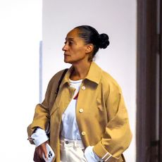 Tracee Ellis Ross wearing a tan trench coat, white tee, white jeans, and white glove flats