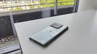 OnePlus 10T phone lying on a white desk with trees and building behind