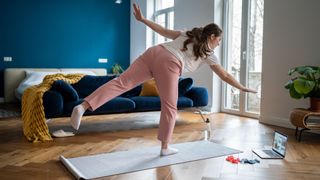 Woman doing yoga for beginners with laptop in living room