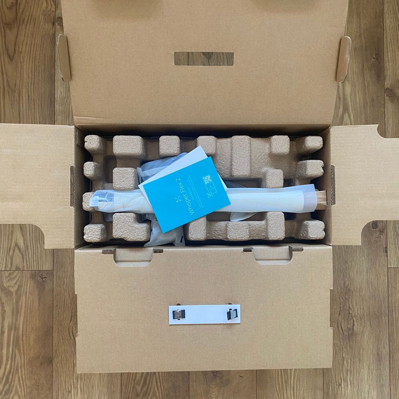 Inner packaging of the Duux Whisper Flex 2 on a wood effect floor