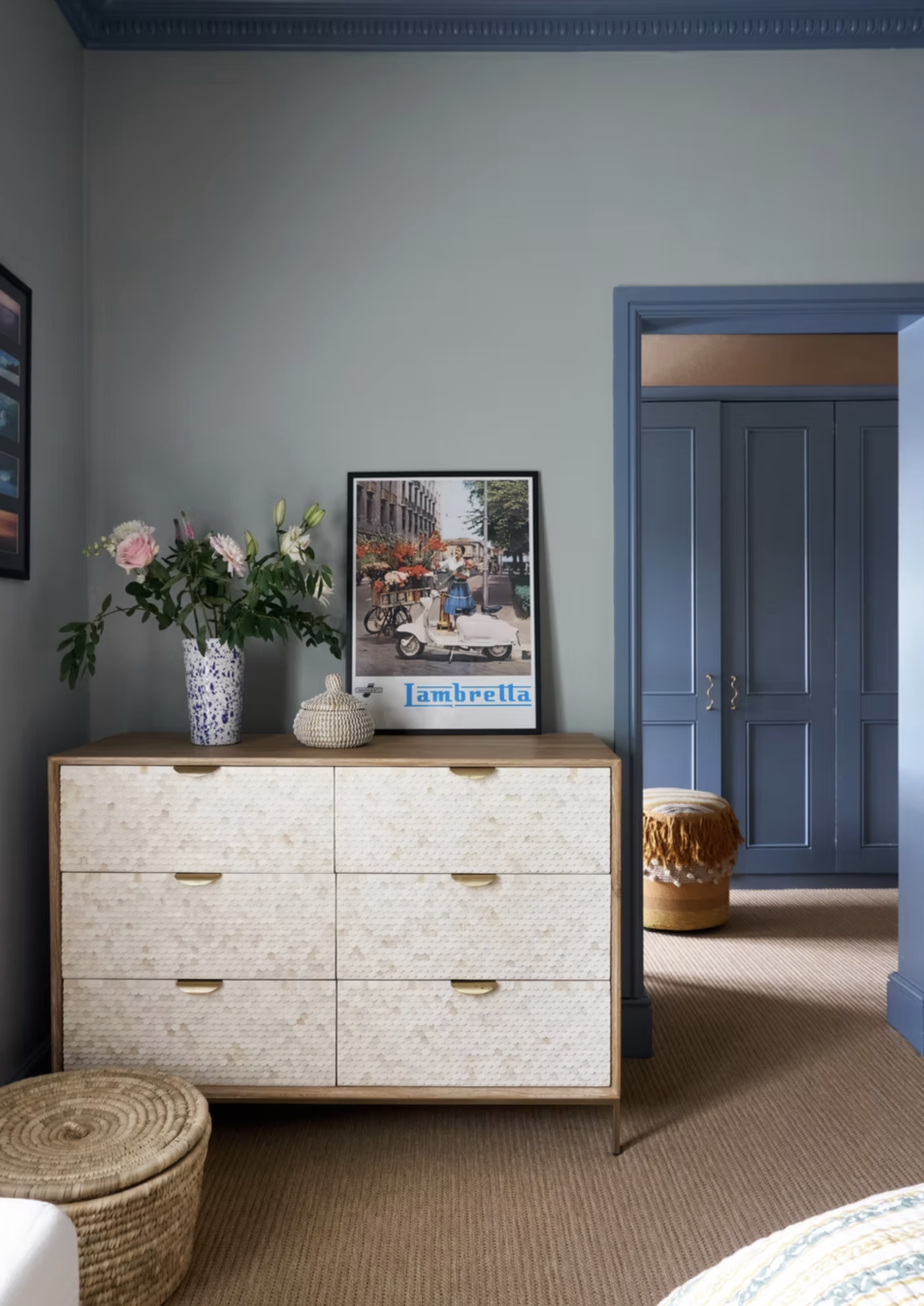 bedroom walls in light blue with dark blue trim with console with vase and artwork, with carpets and jute basket, with blue wardrobe doors