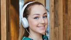 Woman wearing white headphones smiling as she listens to music