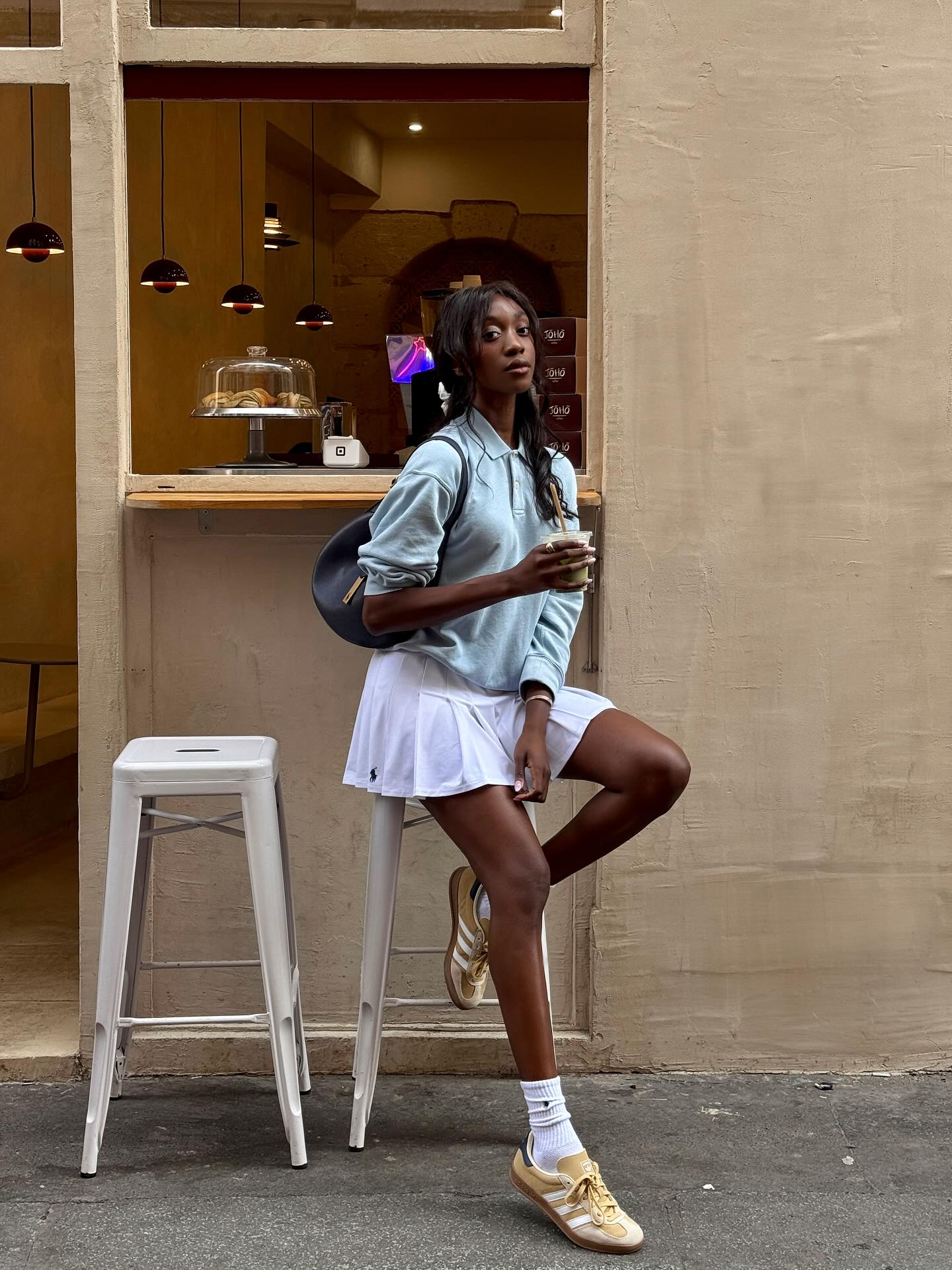 An image of @emmanuellek_ wearing a blue polo shirt with trainers, one of the best lace-up shoes, and a pleated mini skirt.