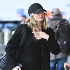 Emily Blunt wearing a black outfit and baseball cap with white sneakers at the airport