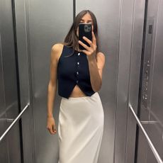 Woman standing in elevator wearing Zara black vest and cream slip skirt.