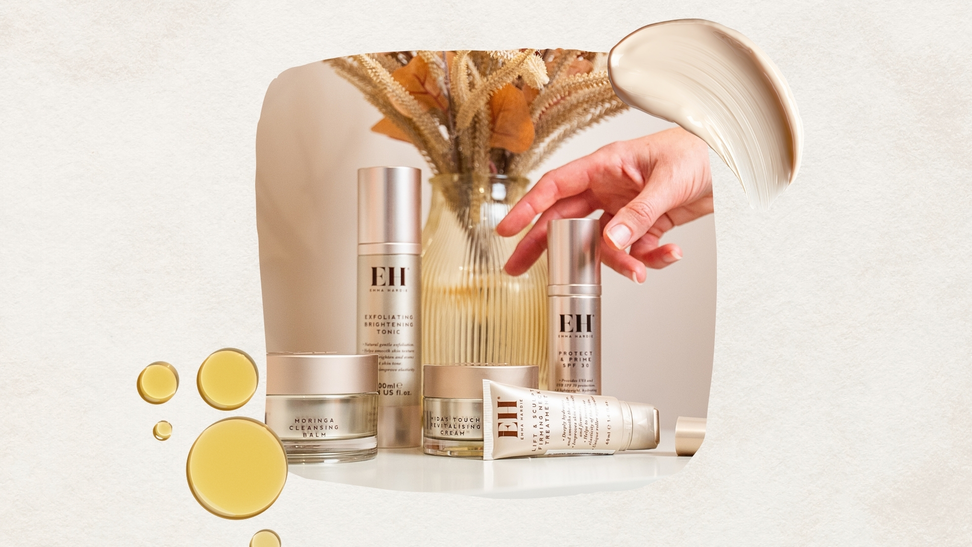 A lifestyle shot featuring some of Emma Hardie's best-sellers arranged in front of a vase of flowers, on a cream background with an oil and cream skincare swatch. 
