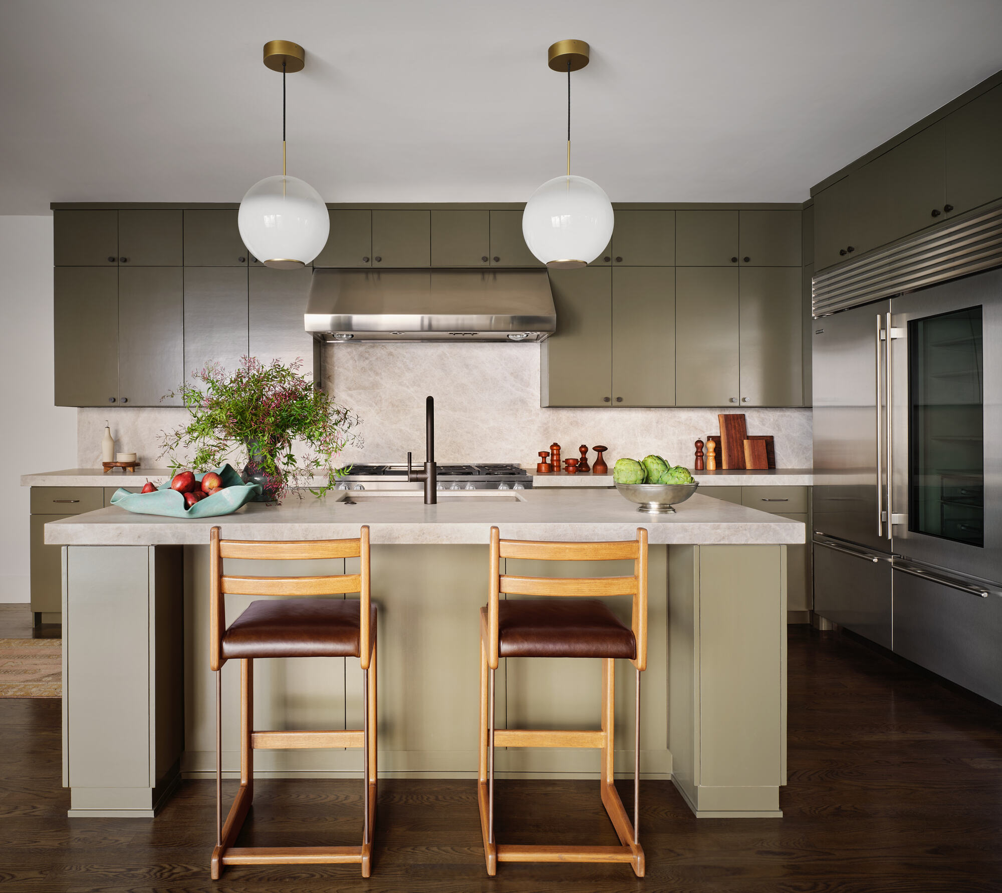 modern kitchen with sage green-gray cabinetry, stone countertops, two pendant lights over the island, two timber barstools