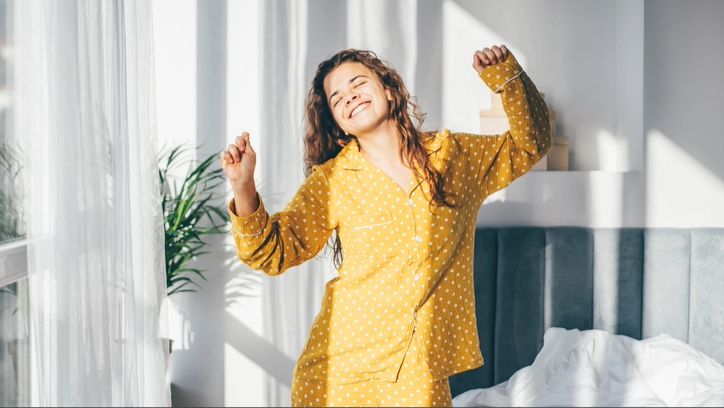 A woman in yellow pyjamas dancing as she wakes up in naturally light room