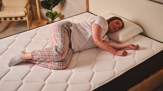 A person lies in a side sleeping position on the Plank Firm mattress, on the Extra Firm side