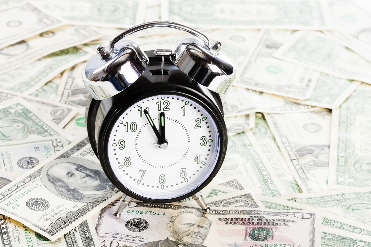 A pile of dollar bills, topped with an old-fashioned alarm clock