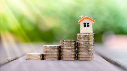 Four progressively taller stacks of coins with a small home sitting on the tallest stack.