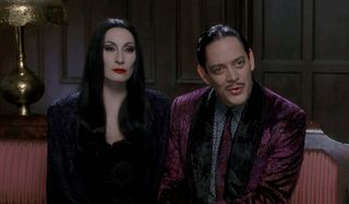 The Addams Family Anjelica Houston and Raul Julia sitting on the couch, in conversation