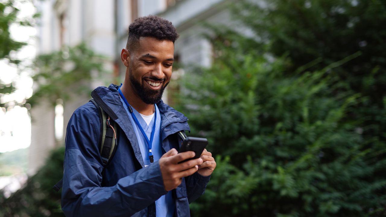 A nurse looks at his phone as he walks outside.