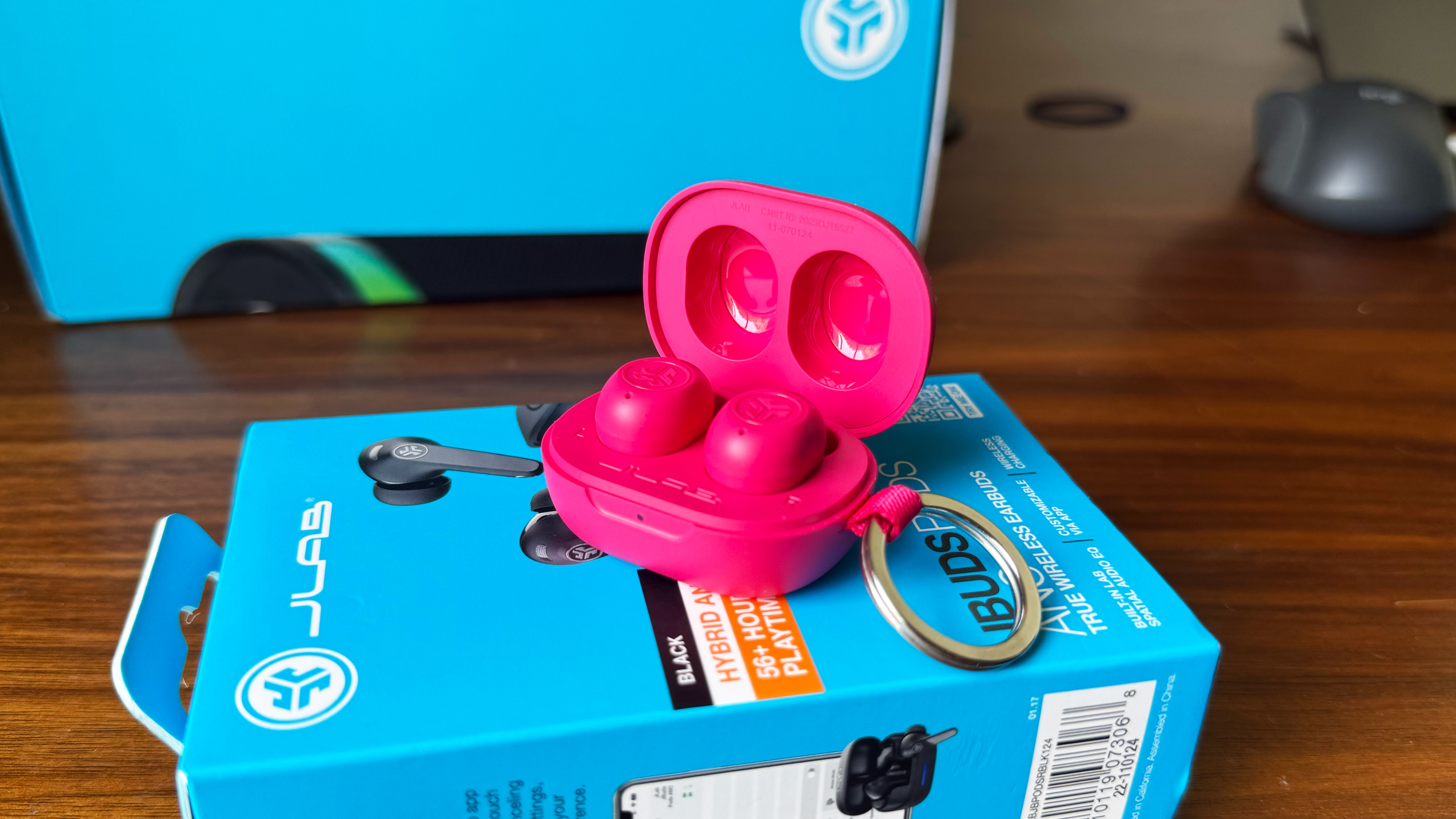 the jlab jbuds mini earbuds in hot pink photographed on top of a bright blue jlab box