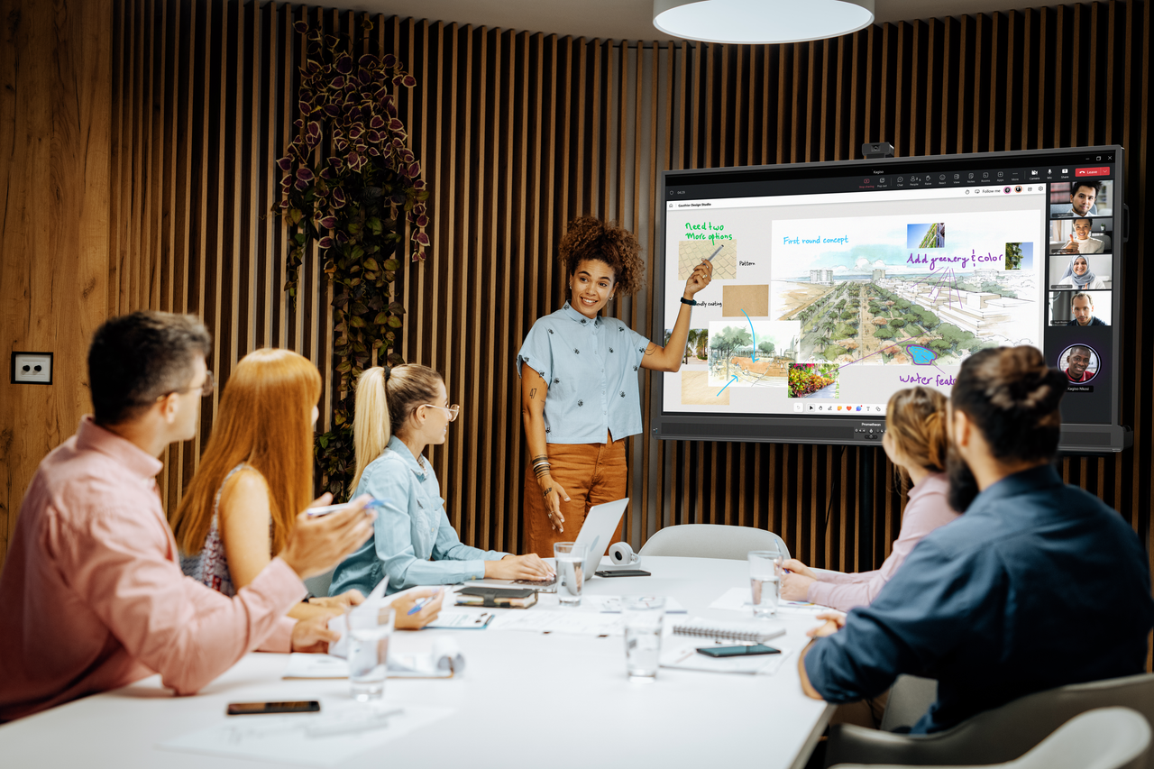 A young, Black women leads a presentation in front of a display in a meeting room.