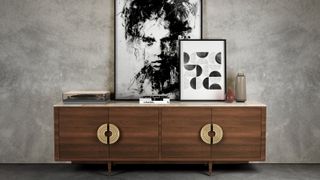 wooden low sideboard with large disc handles with artwork on top in room with grey concrete wall