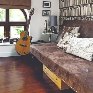 A dark brown suede sofa in a living room with a guitar