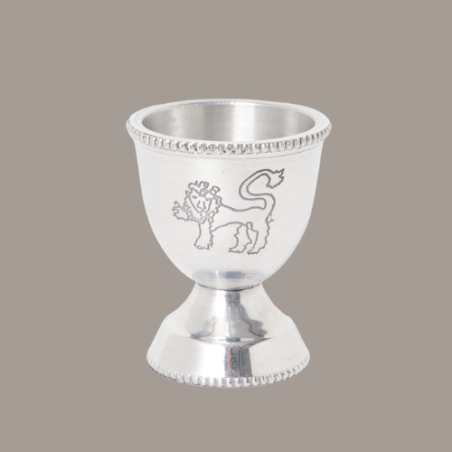 a silver egg cup with a lion on it in front of a gray background.