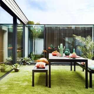 Fake grass lawn with garden table and benches in high fence garden