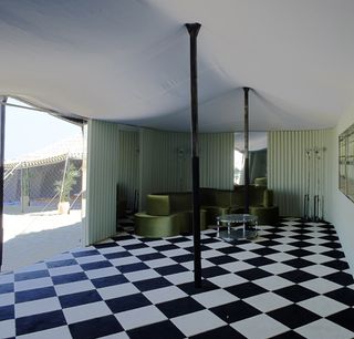 The photo shows the inside of the Prada store tent. Black and white tiles are set on the floor with a satin green sofa in the corner.