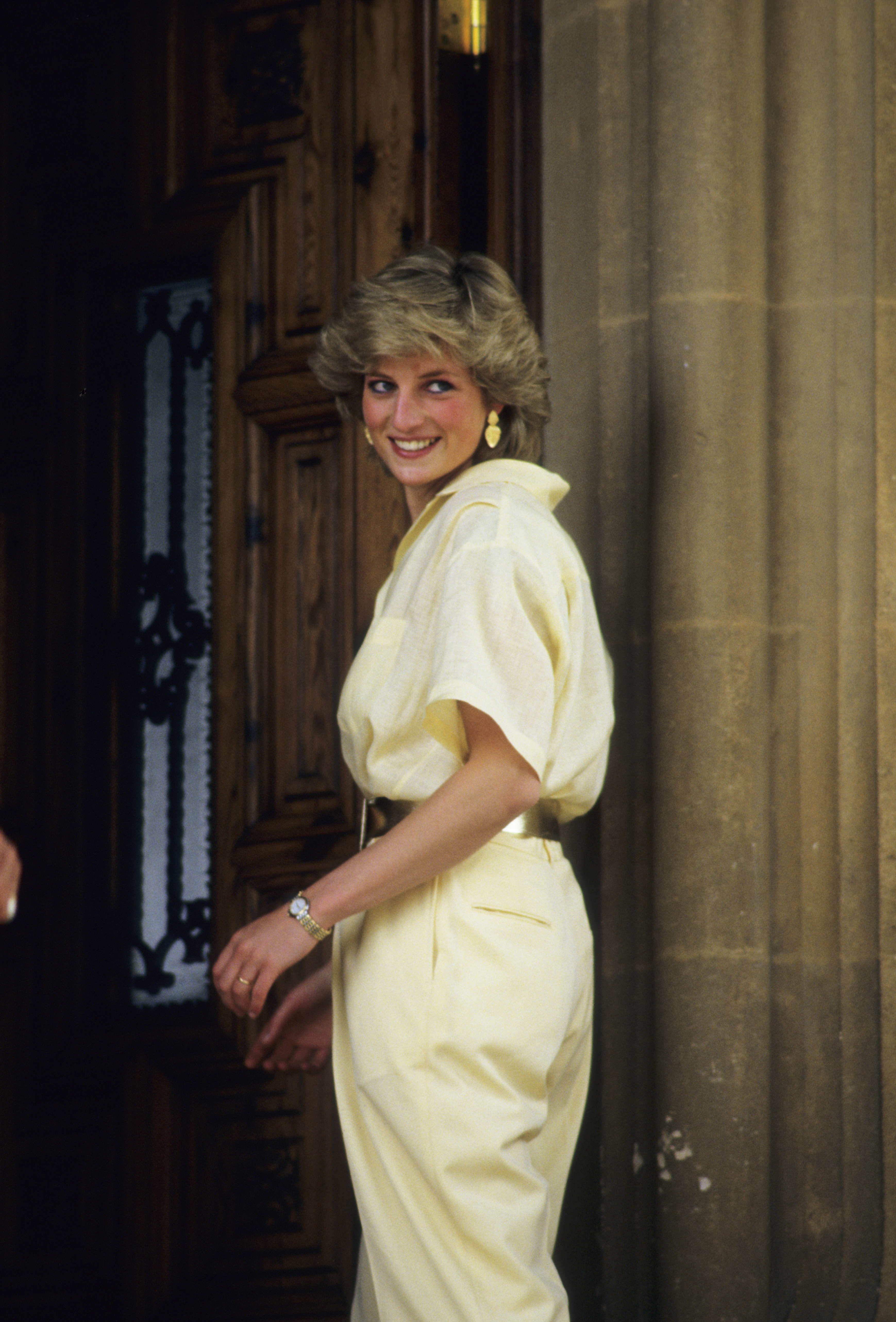 Princess Diana wearing a pale yellow blouse and matching pants standing in a doorway