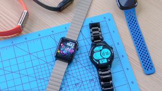 Two Armitron smartwatch models on a blue cutting mat with several Fitbit models off to the side of the image