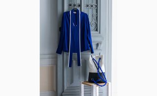 Blue tailored jacket hanging on a door with a hand-free bag on a chair alongside
