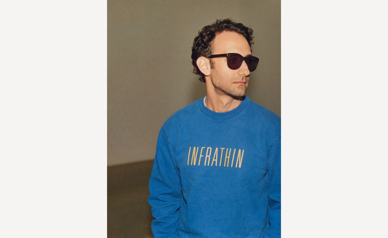 A man wearing sunglasses and a blue jumper with &quot;INFRATHIN&quot; printed on it